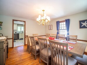 Ein Esszimmer mit Holztisch und Stühlen, einer Kandelaber und Blick in die Küche durch einen offenen Durchgang.