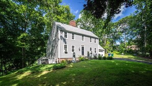 A two-story house with a sloped roof, surrounded by a well-maintained lawn and trees. - Connecticut Beach Home (Old Lyme)