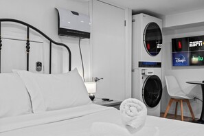 Ein Hotelzimmer mit einem Bett, einer fest installierten Klimaanlage, einer Waschmaschine und einem Fernseher, der Streaming-Dienste anzeigt.
