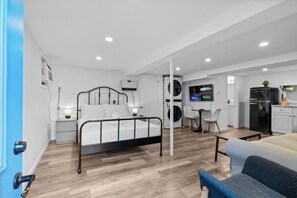 Habitación de hotel moderna con cama, escritorio, silla, televisor, lavadora y refrigerador.