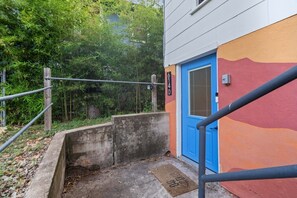 Eine Betontreppe führt zu einer Tür mit blauem Rahmen, umgeben von Grünpflanzen.
