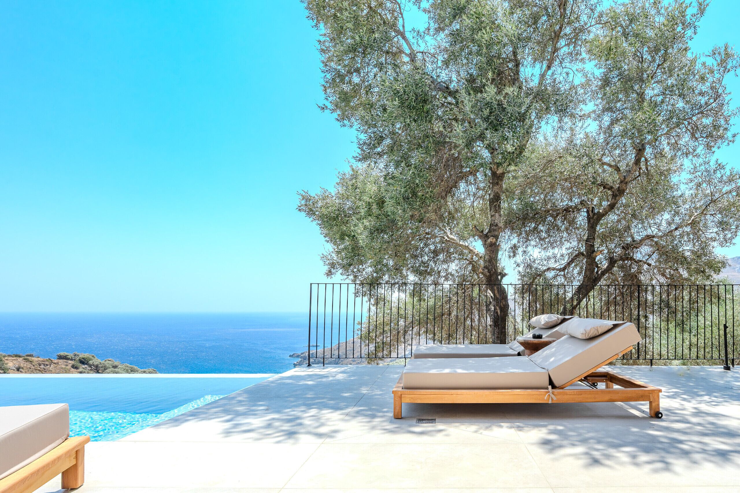 A sunlit outdoor seating area with a pool, overlooking the sea.