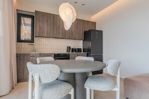 Eine moderne Küche mit einem runden Esstisch, sechs Stühlen, einem Kühlschrank und einem Fenster mit Vorhängen.