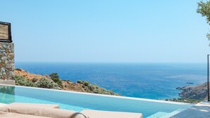 A pool with a view of the sea, a stone wall, and a lounge area with cushions. - Metatulia 8 (Agios Vasileios)