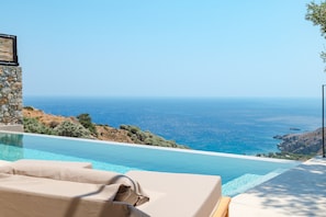 Ein Pool mit Meerblick, eine Steinsäule und eine Lounge-Bereich mit Kissen.