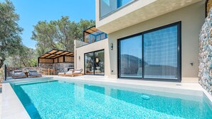 A modern outdoor swimming pool with clear blue water, surrounded by lounge chairs and a stone wall. - Metatulia 8 (Agios Vasileios)