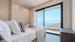 A hotel room with a bed, pillows, a view of the sea, and a large window. - Metatulia 8 (Agios Vasileios)