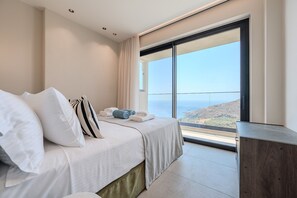 Ein Hotelzimmer mit Bett, Kissen und Meerblick, inklusive großem Fenster.