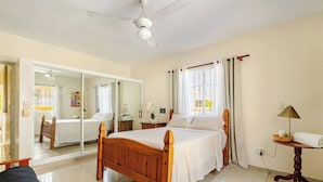 Un dormitorio con cama de madera, ventilador de techo, ventana con cortinas, mesita de noche y espejo.