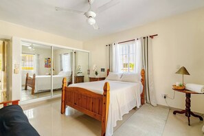 Ein Schlafzimmer mit einem Holzbett, Deckenventilator, einem Fenster mit Vorhängen, einem Nachttisch und einem Spiegel.