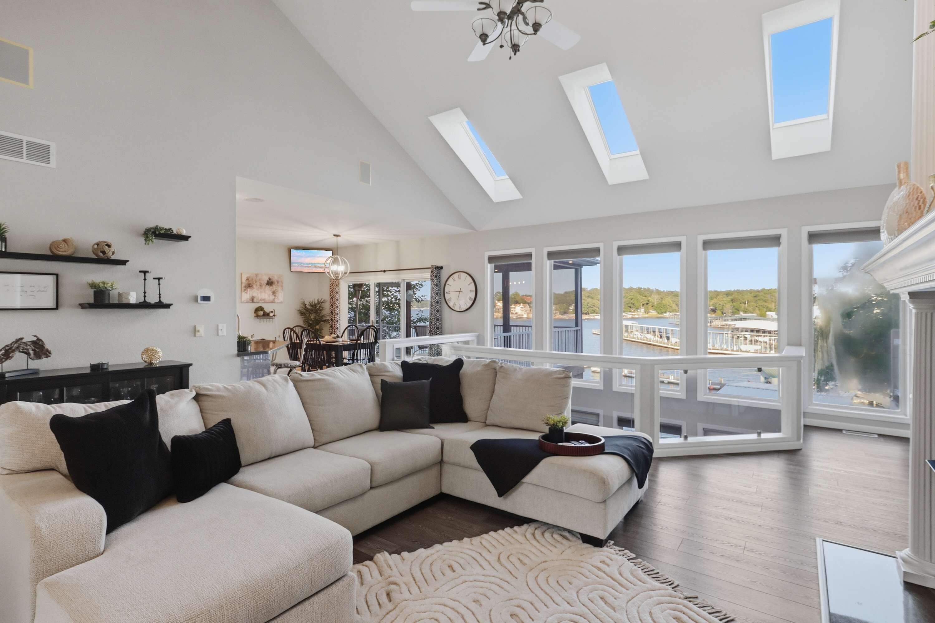 A spacious living room with a large sectional sofa, a dining area, and a view of a body of water through large windows.