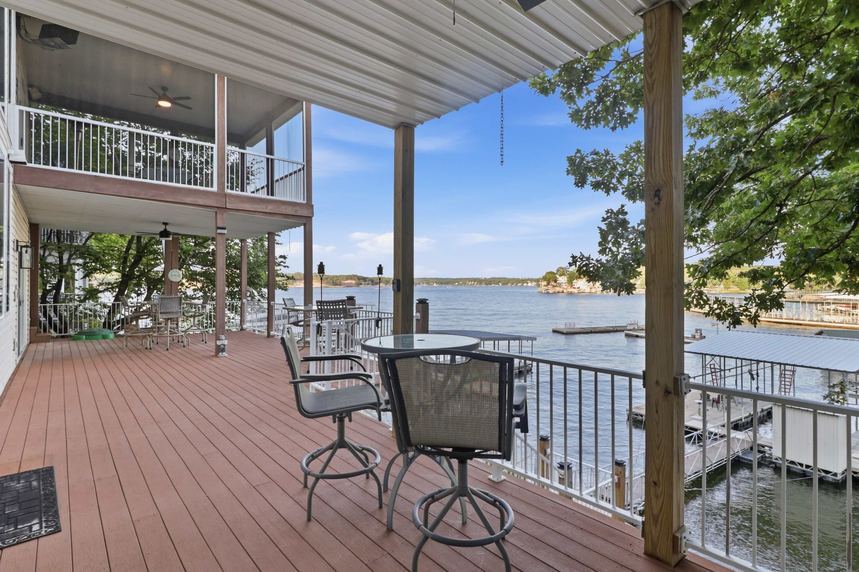 A covered outdoor deck with a table and chairs, overlooking a body of water.