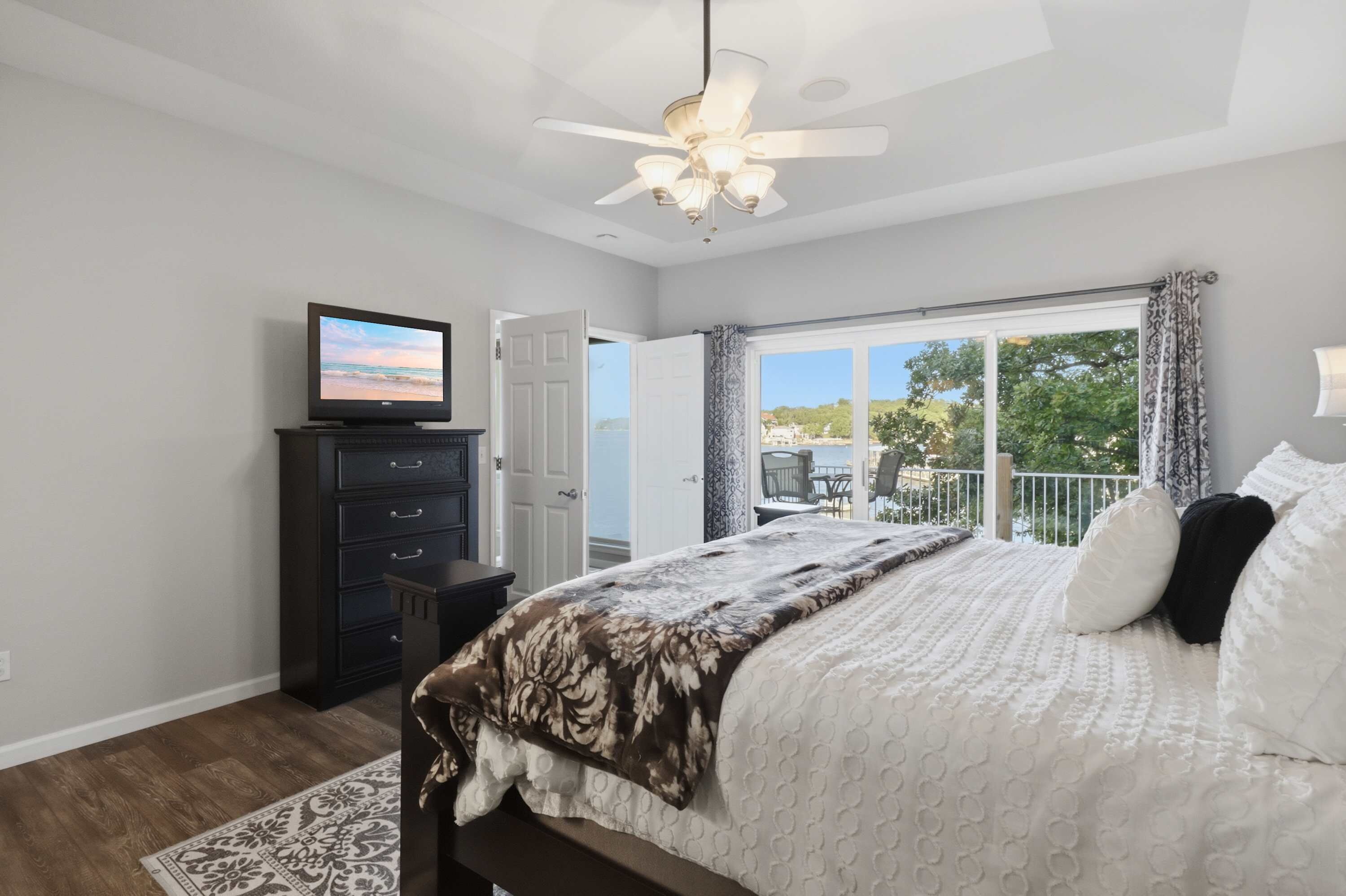 A bedroom with a bed, a dresser, a television, and a ceiling fan.