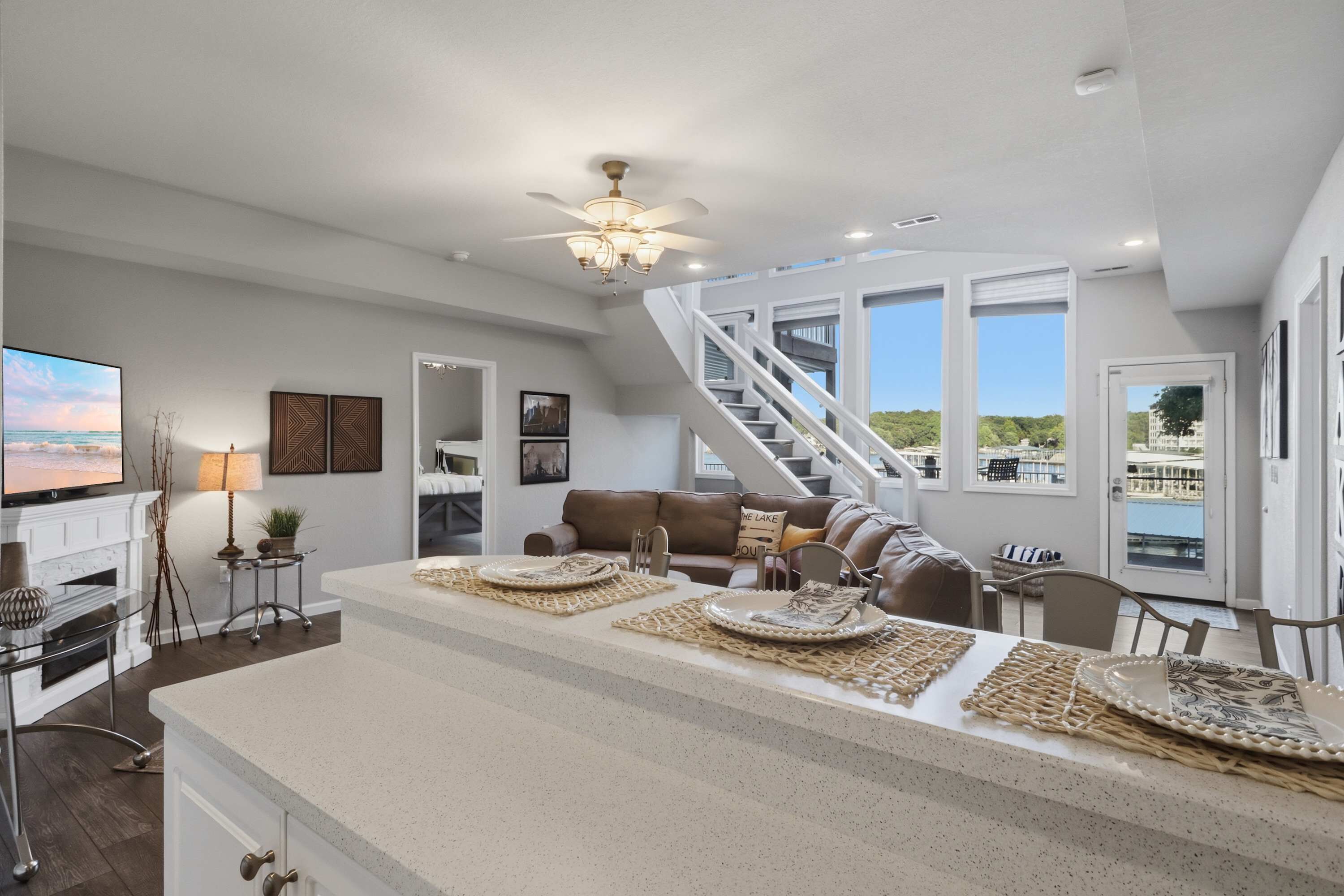 A spacious living area with a large island, a staircase, and a view of the outdoors.