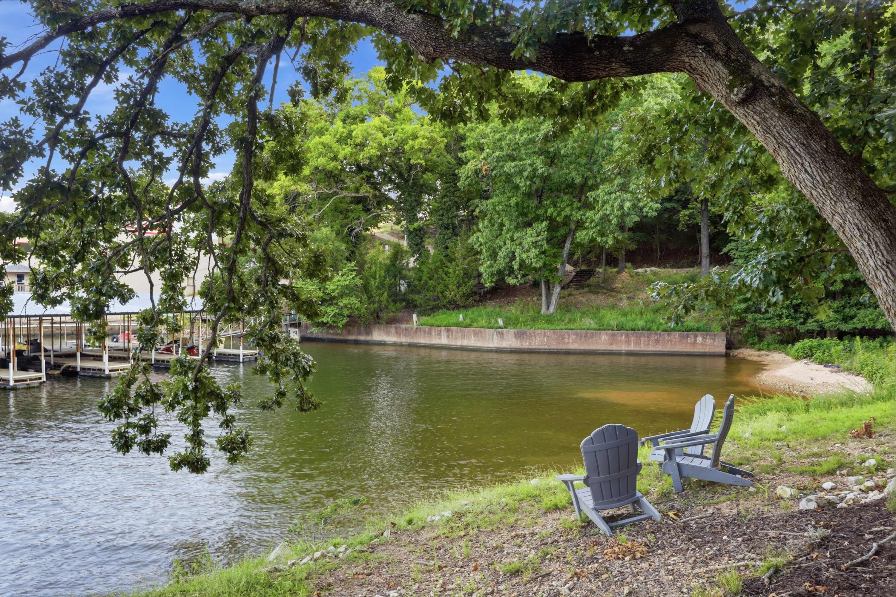 A lakeside view with docked boats, a wooden pier, and two Adirondack chairs.