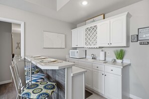 A modern kitchen with white cabinetry, a microwave, a sink, and a dining area with a chair and table. - Osage Beach, 4b, Private cove, sleeps 10 (Osage Beach)