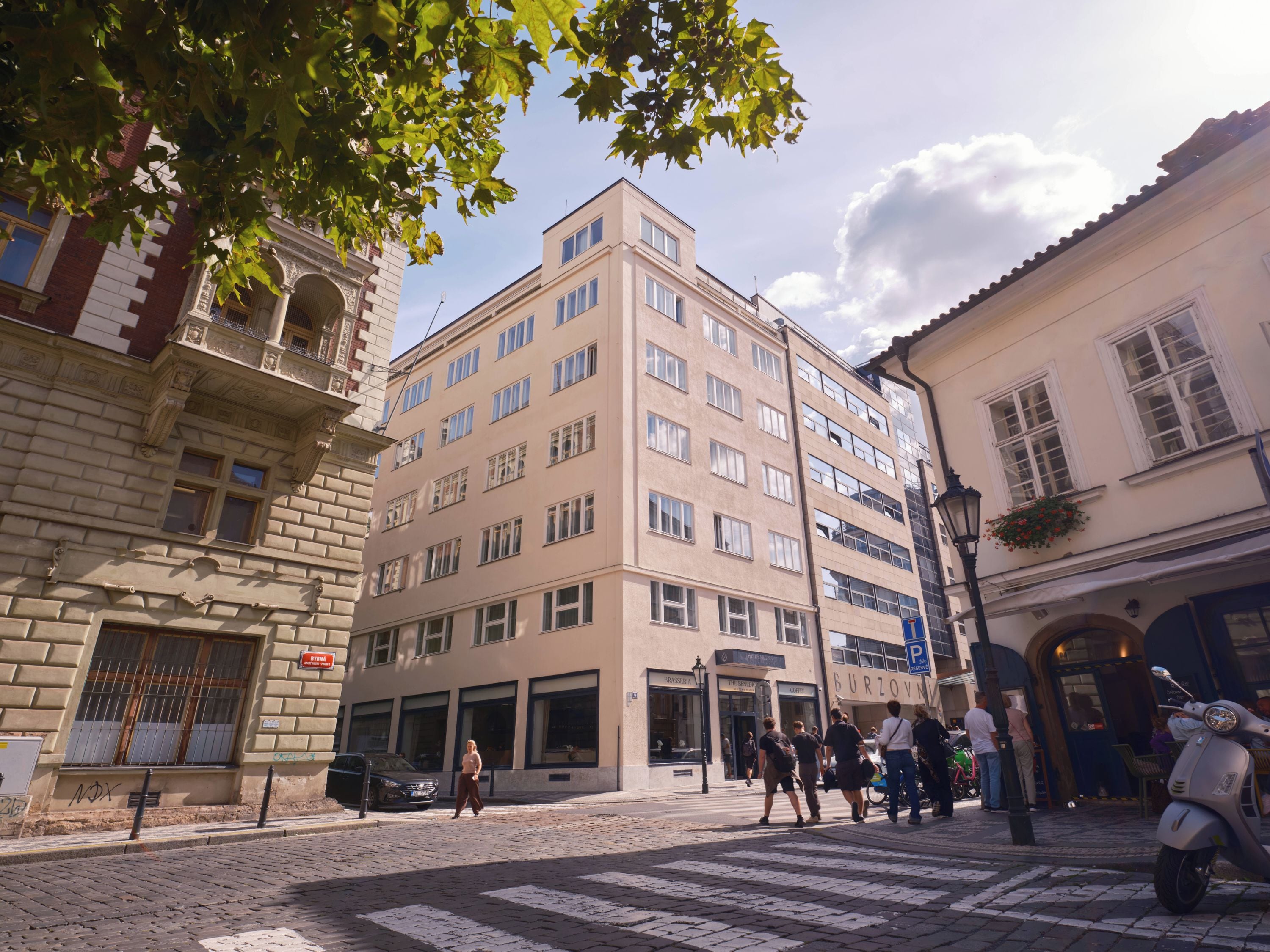 Ein mehrstöckiges Gebäude mit einer Mischung aus Baustilen, darunter ein Eckgebäude mit aufwendiger Gestaltung und ein modernes Gebäude mit großen Fenstern.