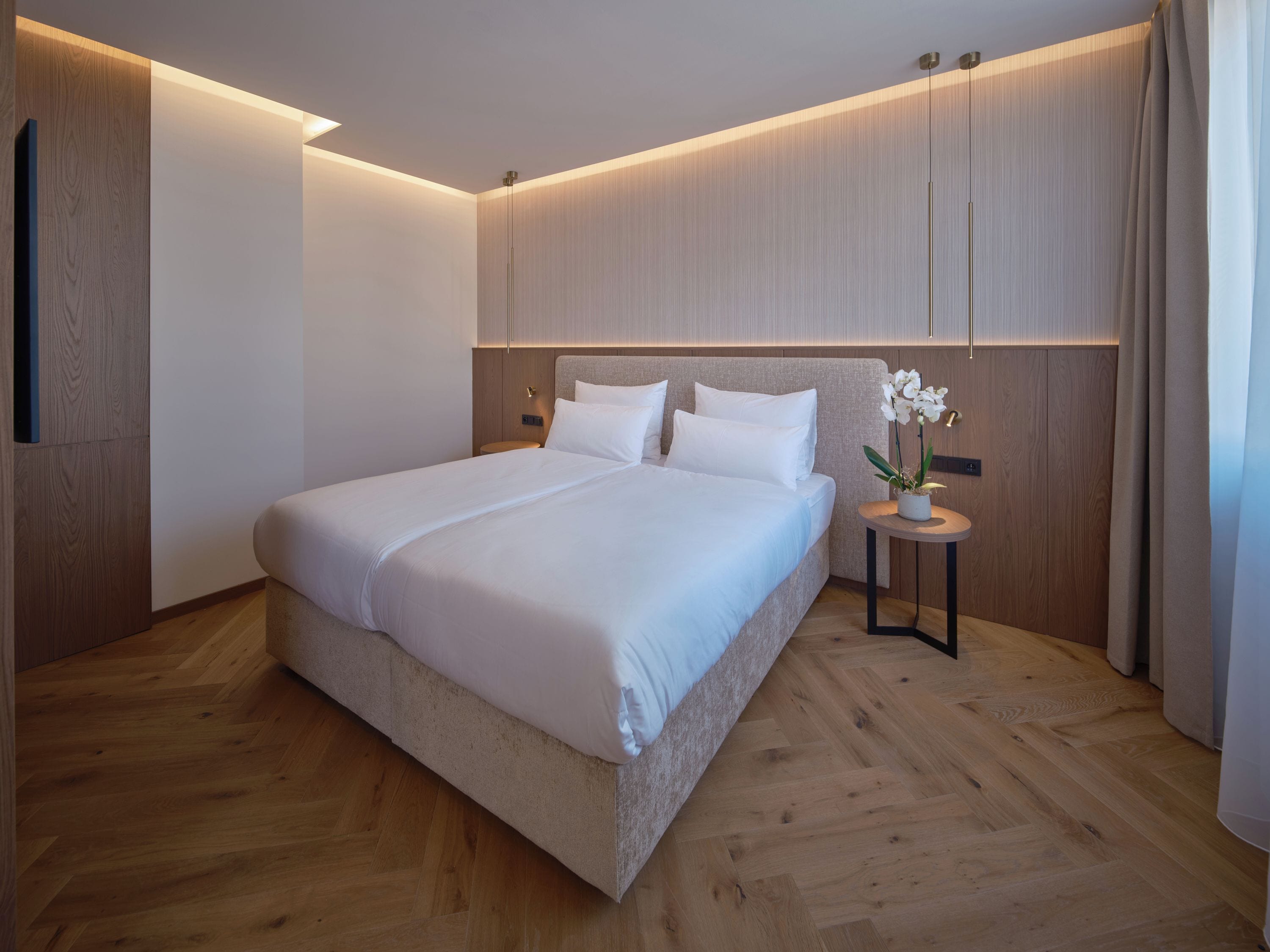 Un dormitorio moderno con una cama grande, una mesita de noche con un jarrón y paneles de madera en las paredes.