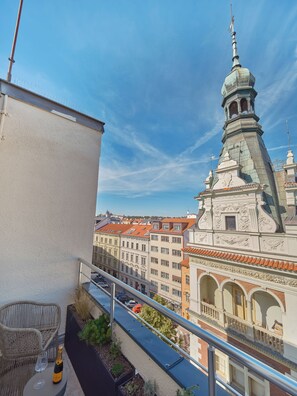 A balcony with a view of a historic building with a tower, a wicker chair, and a bottle of champagne. - The Benedict Hotel Old Town Prague (Prague)