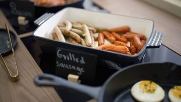 A buffet table with labeled containers of grilled sausages and bacon.