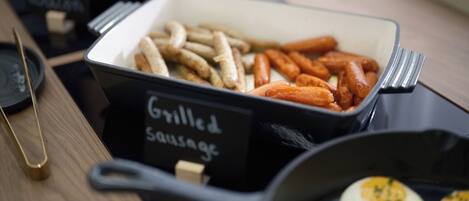 A buffet table with labeled containers of grilled sausages and bacon.