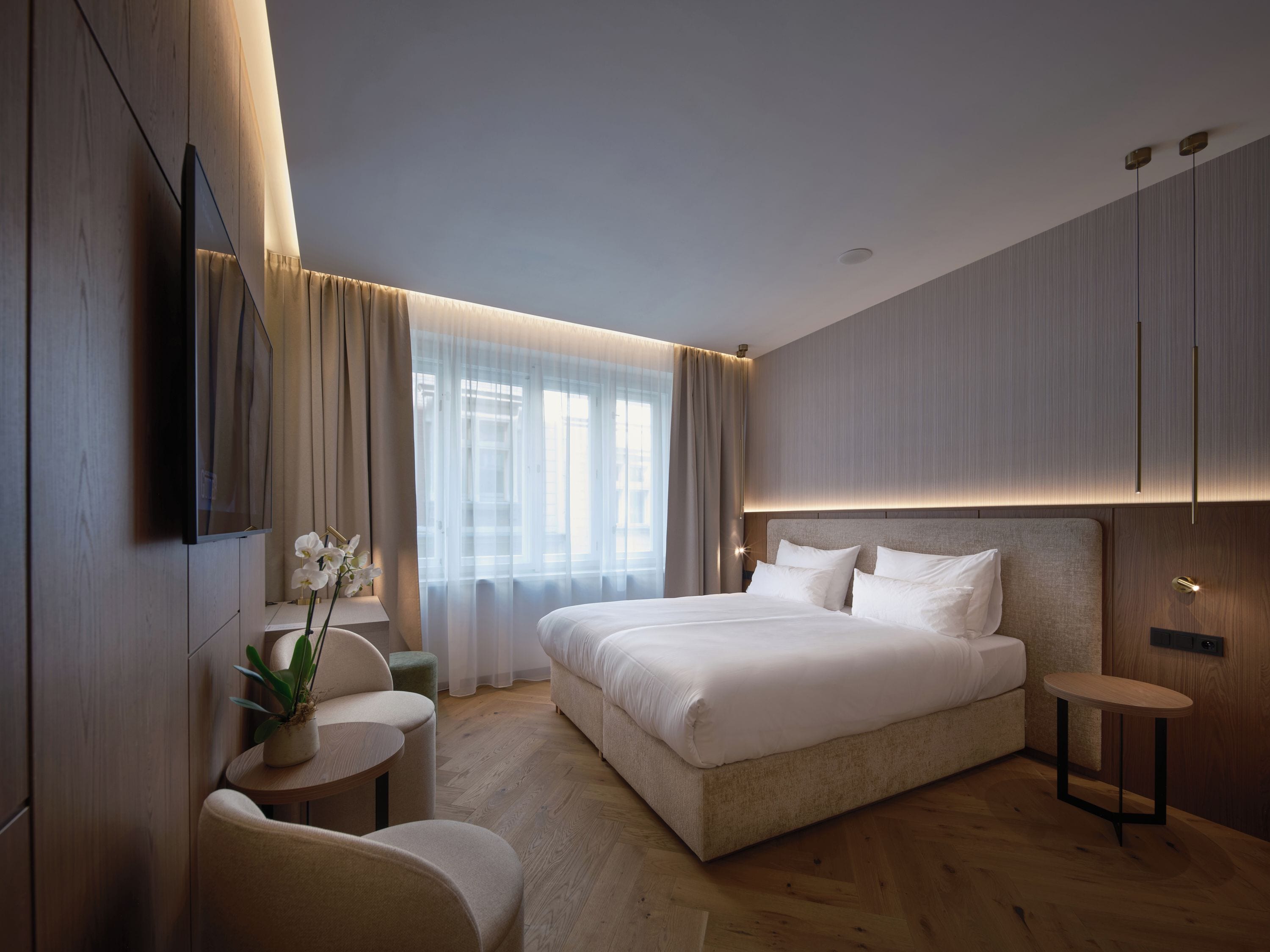 Ein modernes Hotelzimmer mit einem großen Bett, einem Fernseher, einem kleinen Tisch mit einer Pflanze und Blick auf die Stadt durch das Fenster.