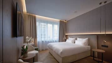 Ein modernes Hotelzimmer mit einem großen Bett, einem Fernseher, einem kleinen Tisch mit einer Pflanze und Blick auf die Stadt durch das Fenster.