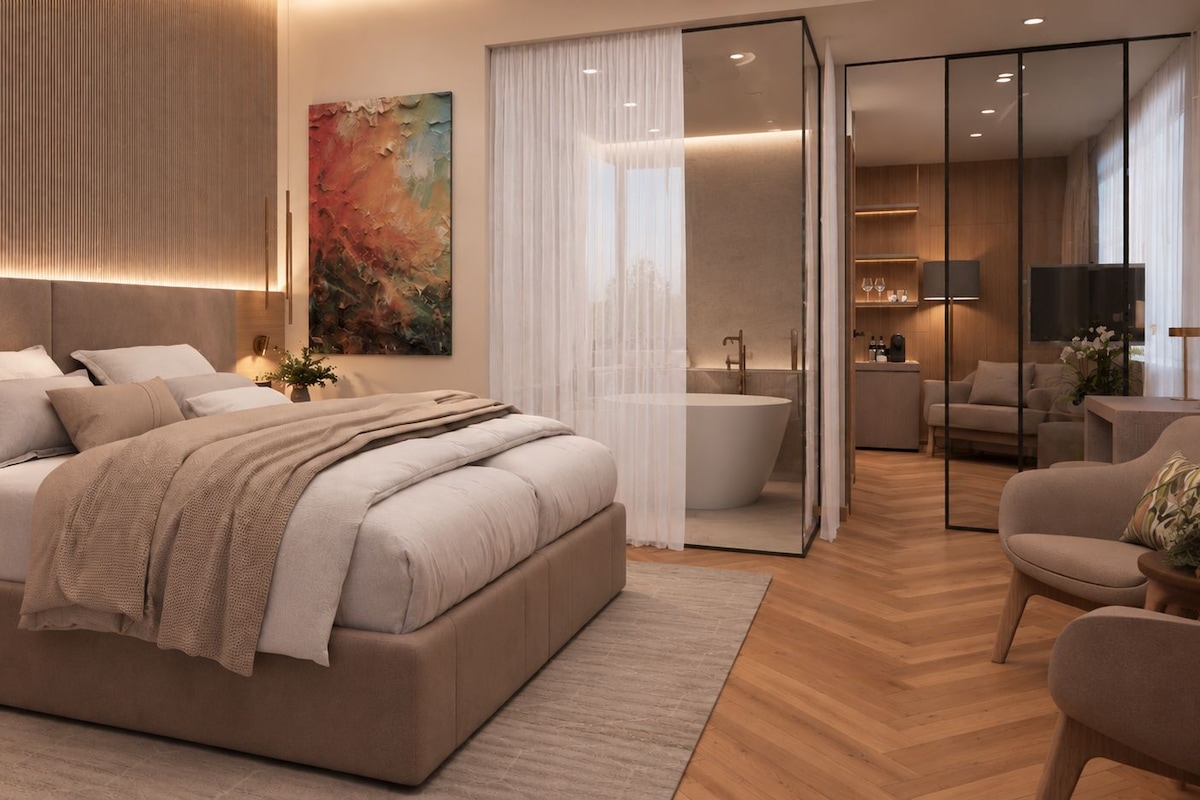 A modern bedroom with a large bed, a bathroom with a bathtub, and a living area with a sofa and a TV.