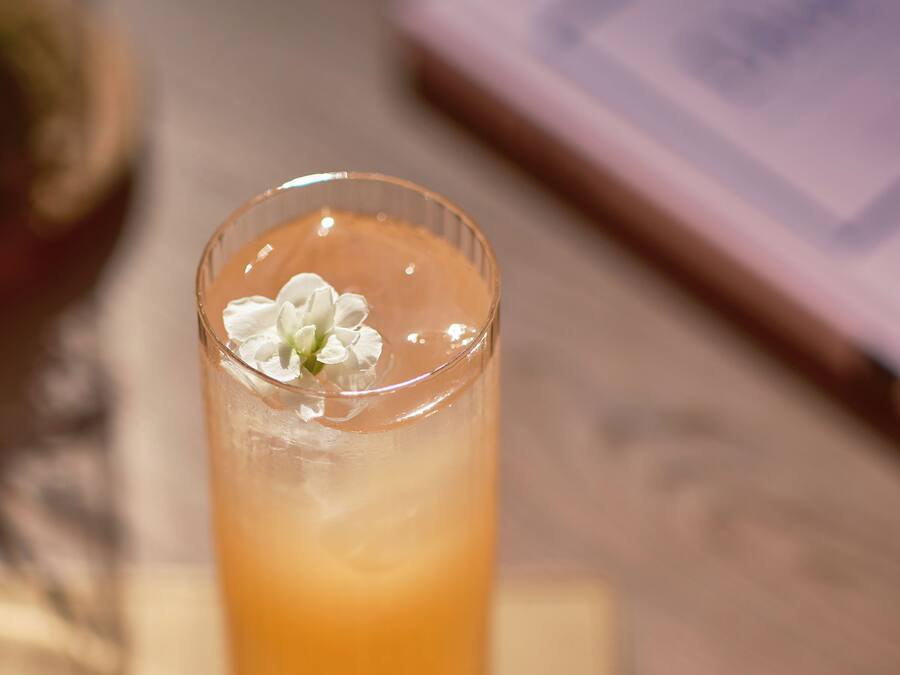 A clear glass with a beverage and a white flower on a reflective surface.