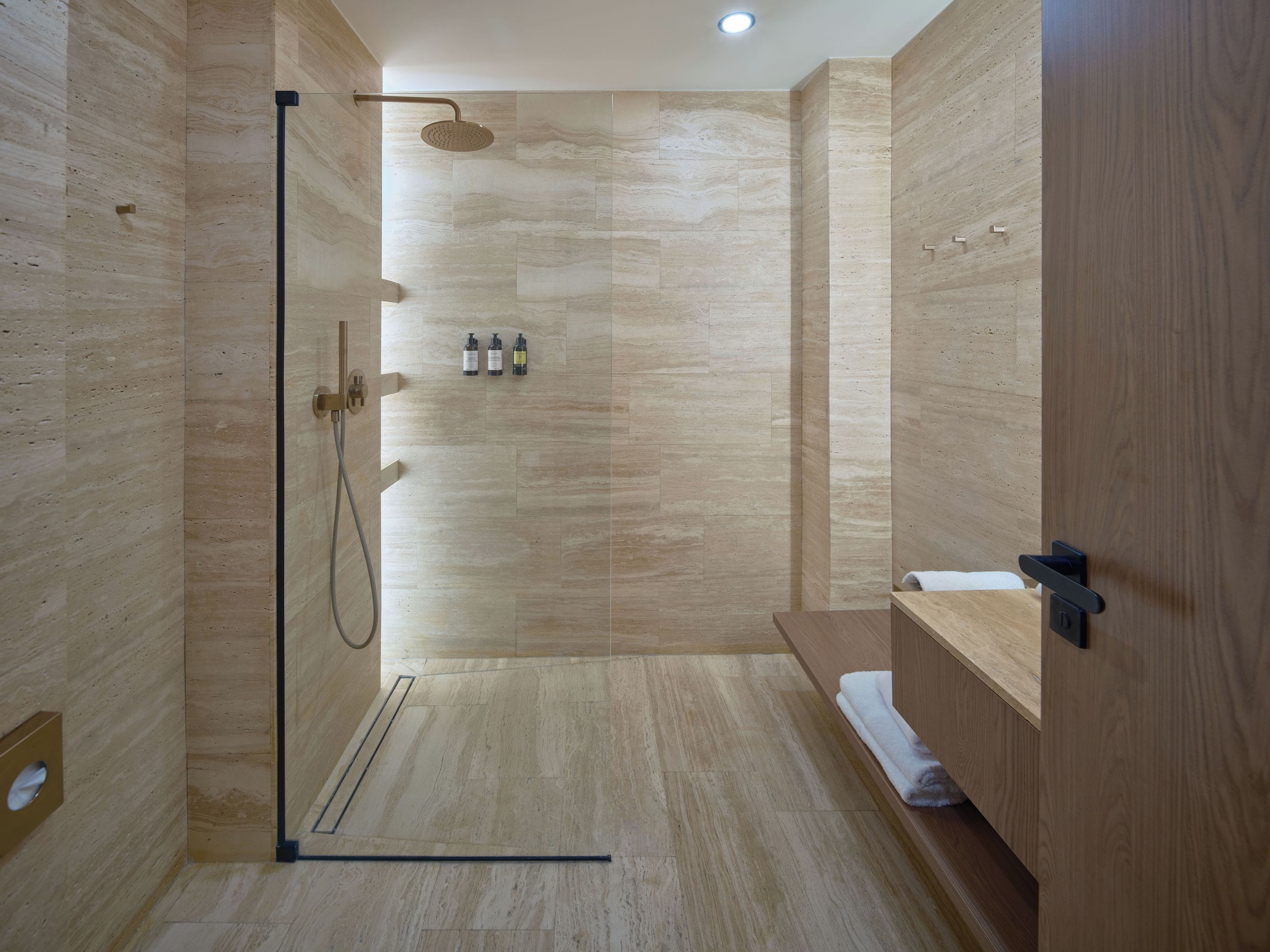 Un área de ducha moderna con puerta de vidrio, cabezal de ducha de mano y panel de control en la pared.