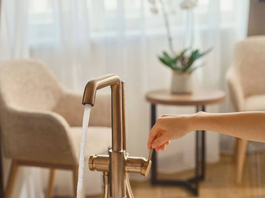 Una mano abriendo un grifo con agua corriendo hacia una bañera.