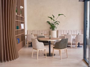 Un interior moderno con una mesa redonda rodeada de sillas, una planta en maceta grande y una estantería de madera.