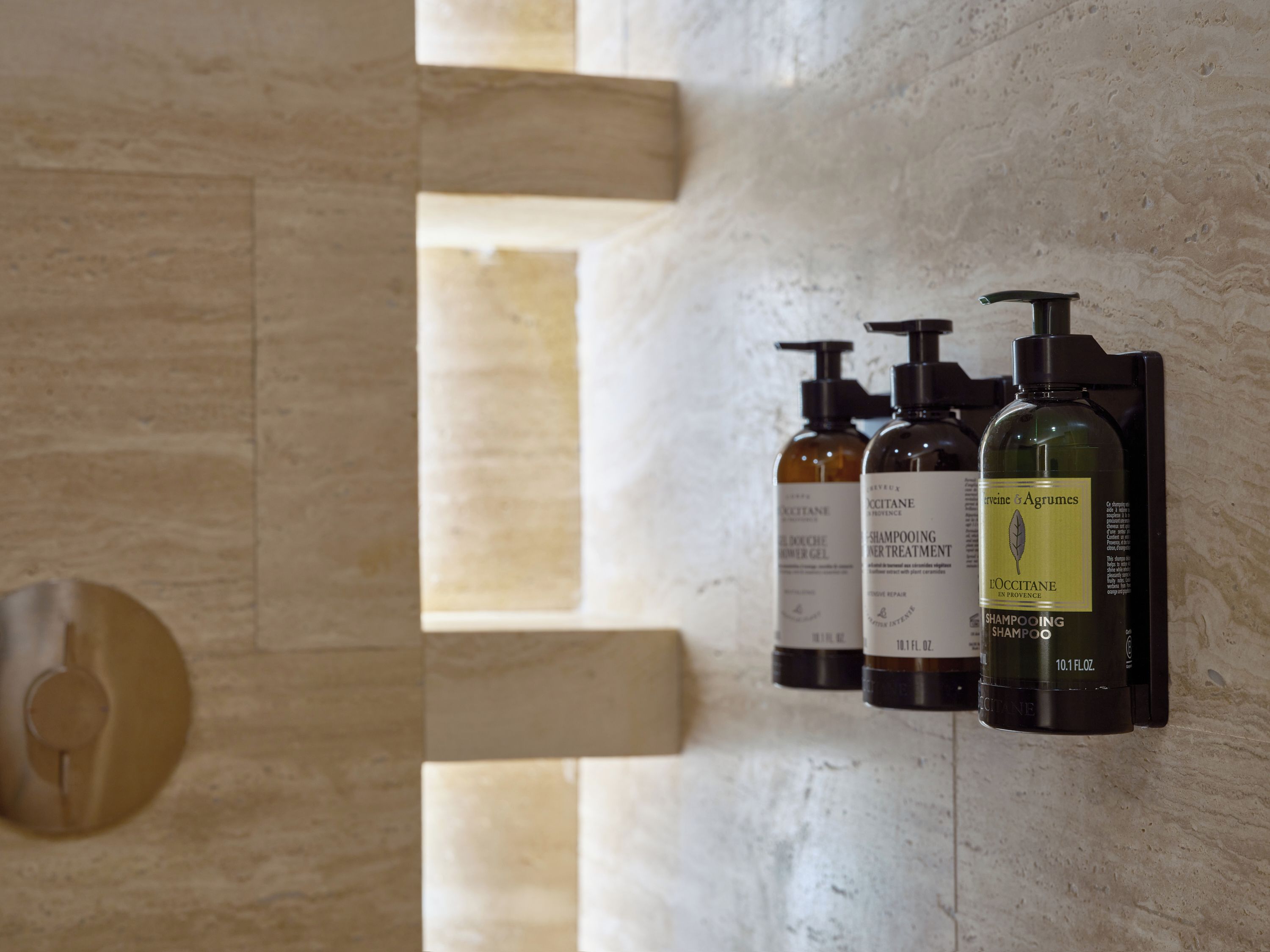 Dispensador na parede com três frascos de shampoo.