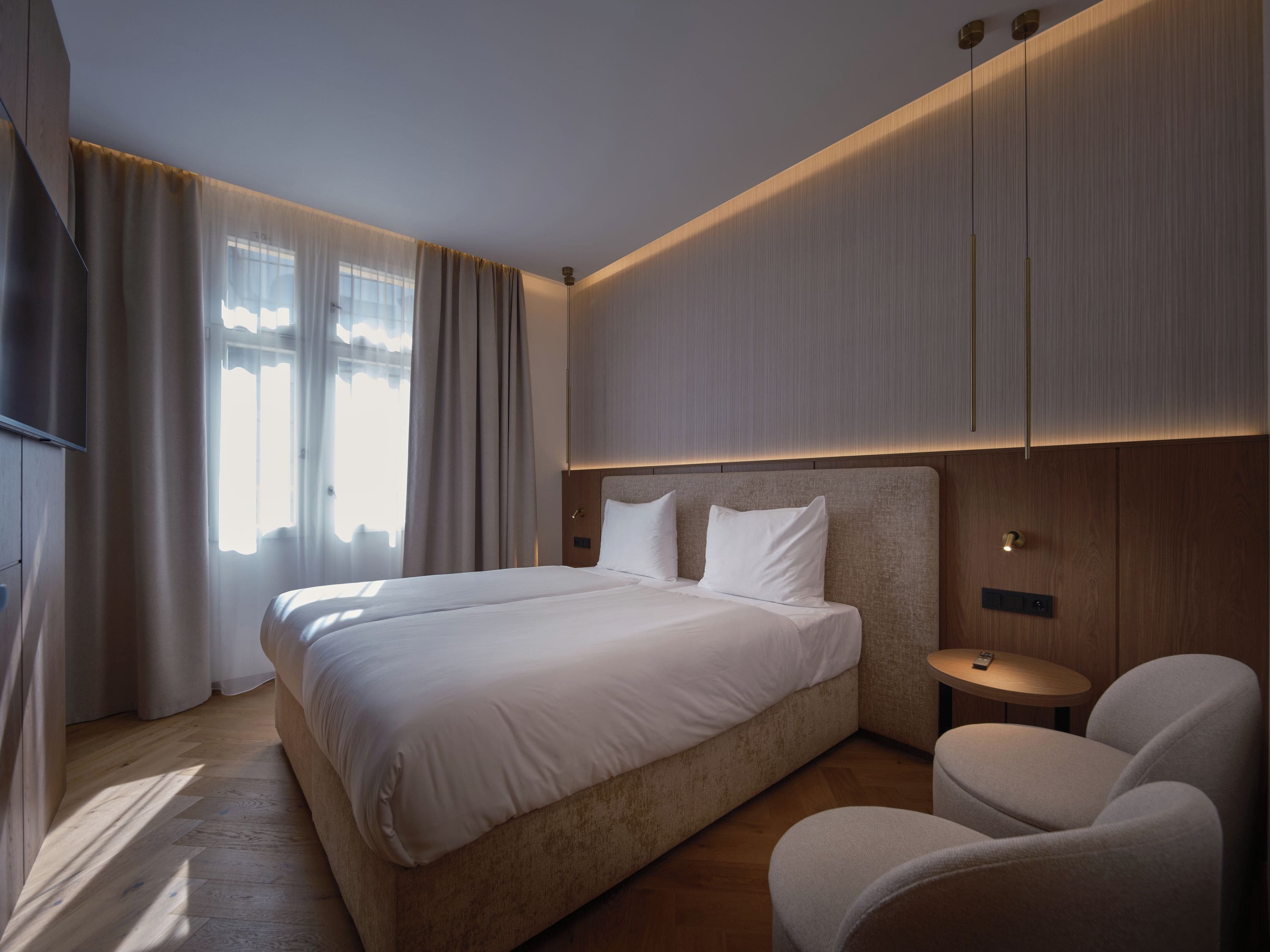 A modern hotel room with a large bed, a bedside table, a chair, and a TV mounted on the wall.