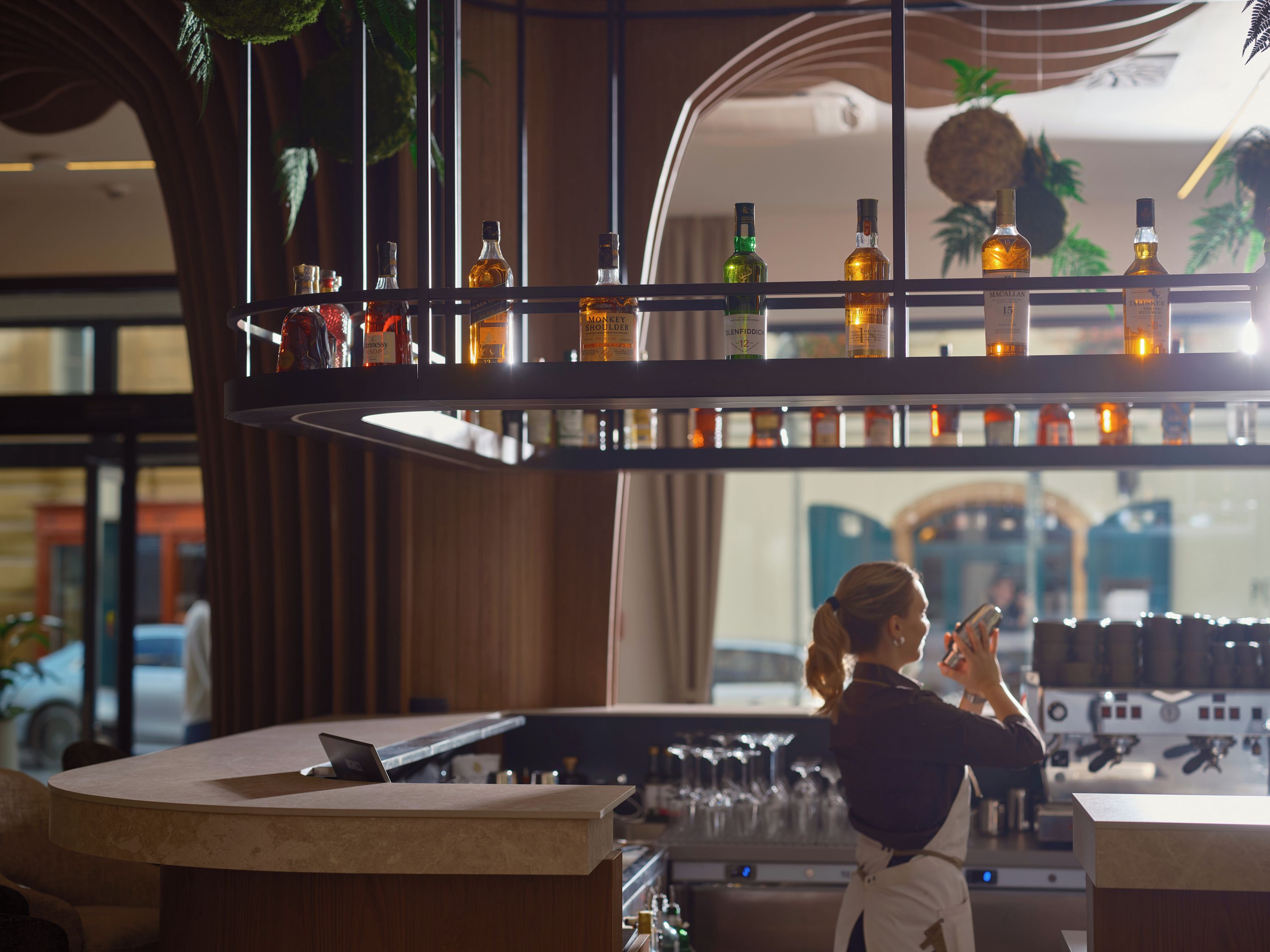 Een bar met drankflessen op planken, een toog en een persoon achter de bar.