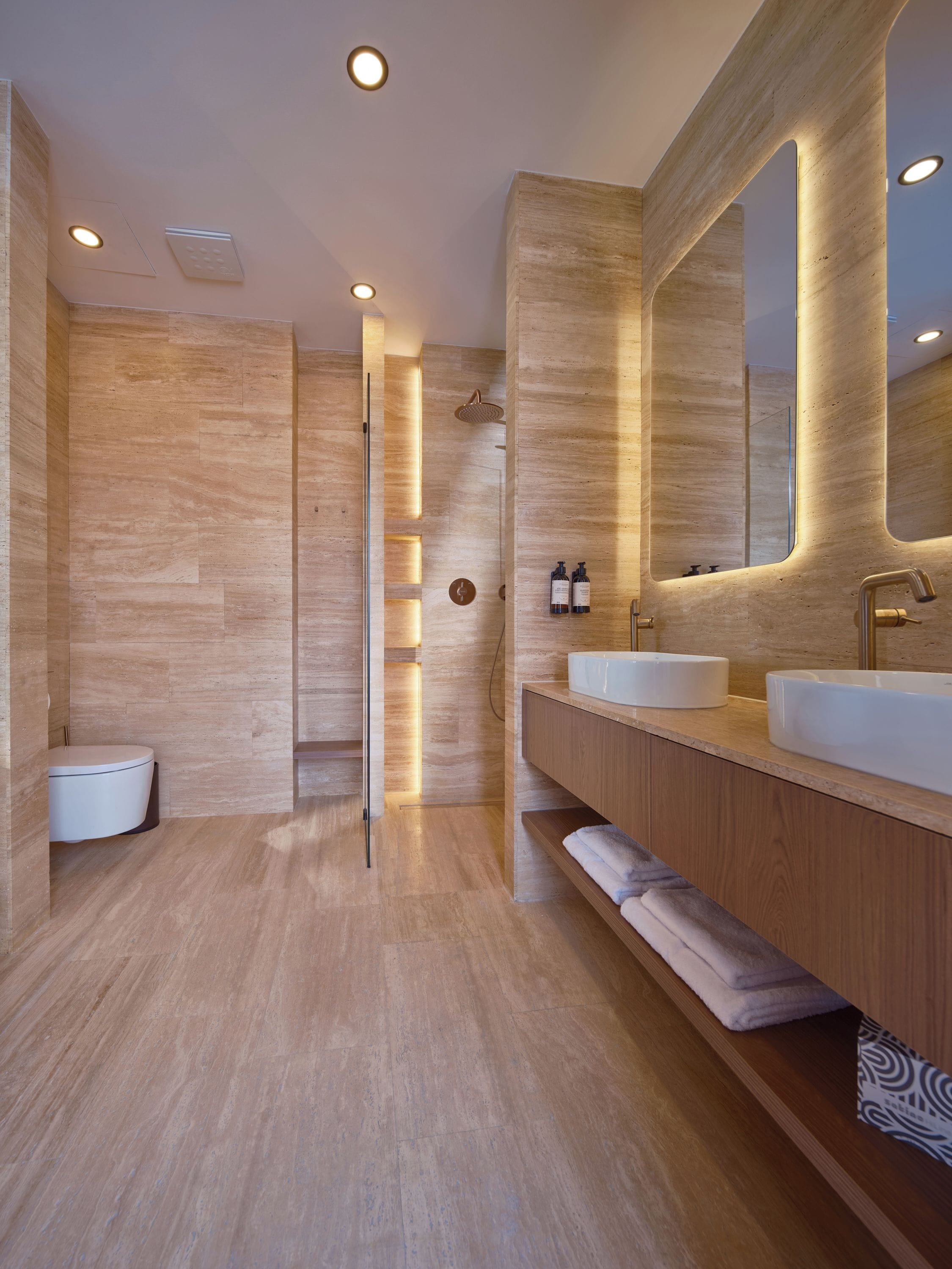A modern bathroom with a wooden floor, two sinks, a large mirror, and a shower area.