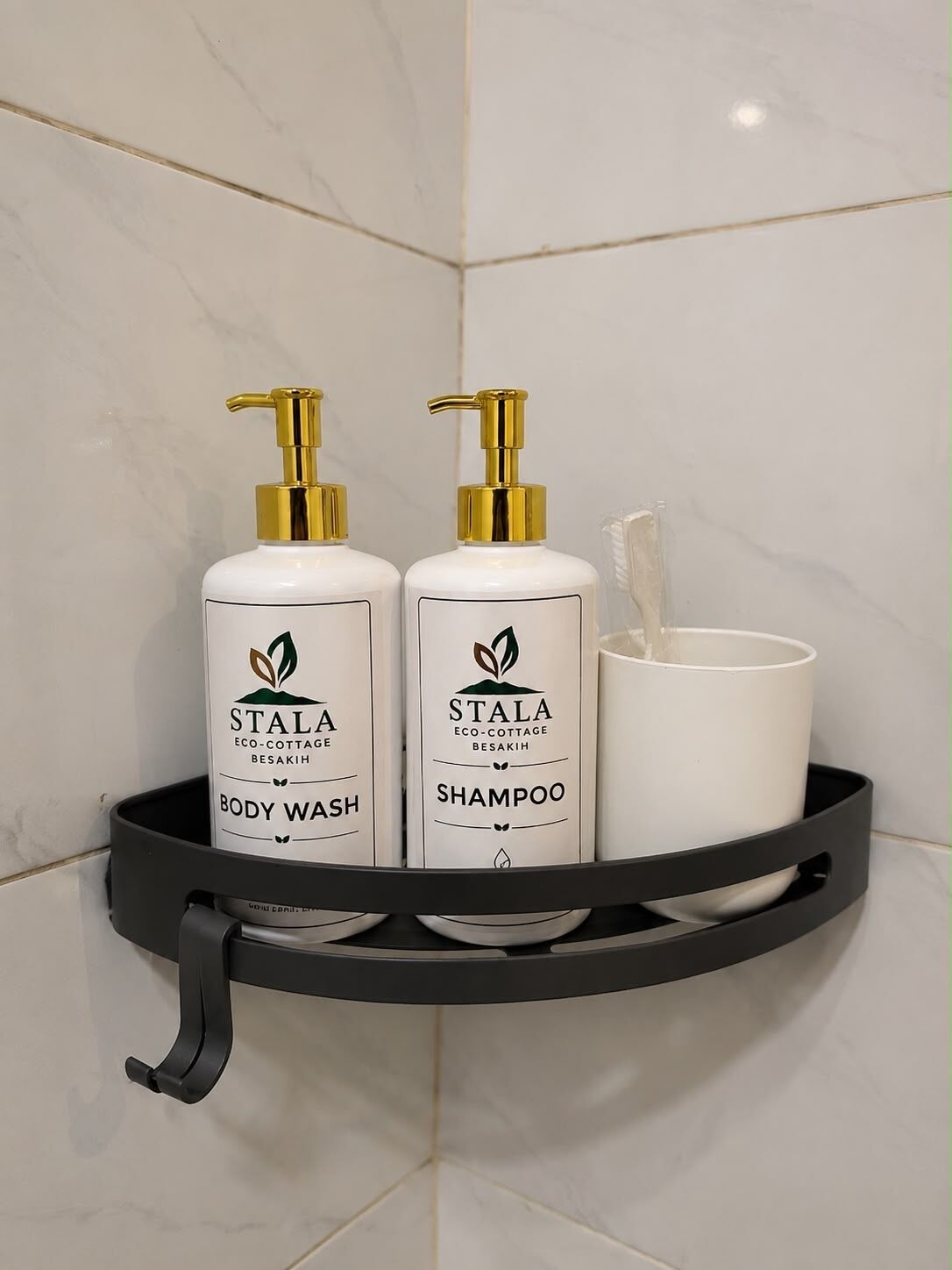 A bathroom shelf with two bottles of Stala body wash and shampoo, and a white cup.