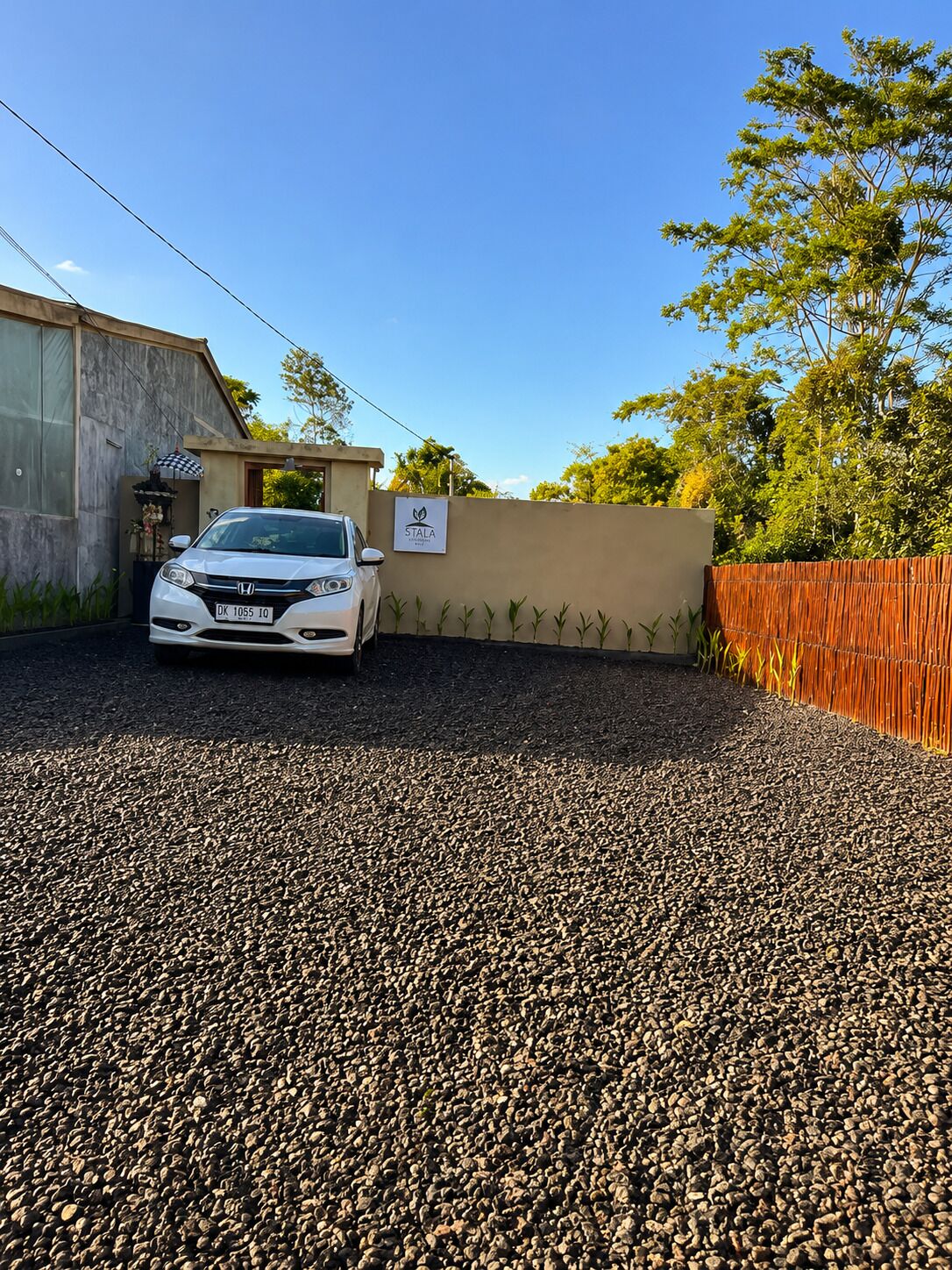 A white car parked in a gravel driveway with a house in the background.
