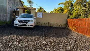 A white car parked in a gravel driveway with a house in the background.