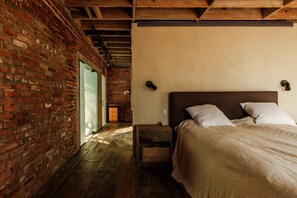 A room with a brick wall, a wooden ceiling, a bed with white bedding, and a small wooden nightstand. - Luxury 3BR Ocean View Home with Pool -  Featured in The New York Times! (Los Angeles)