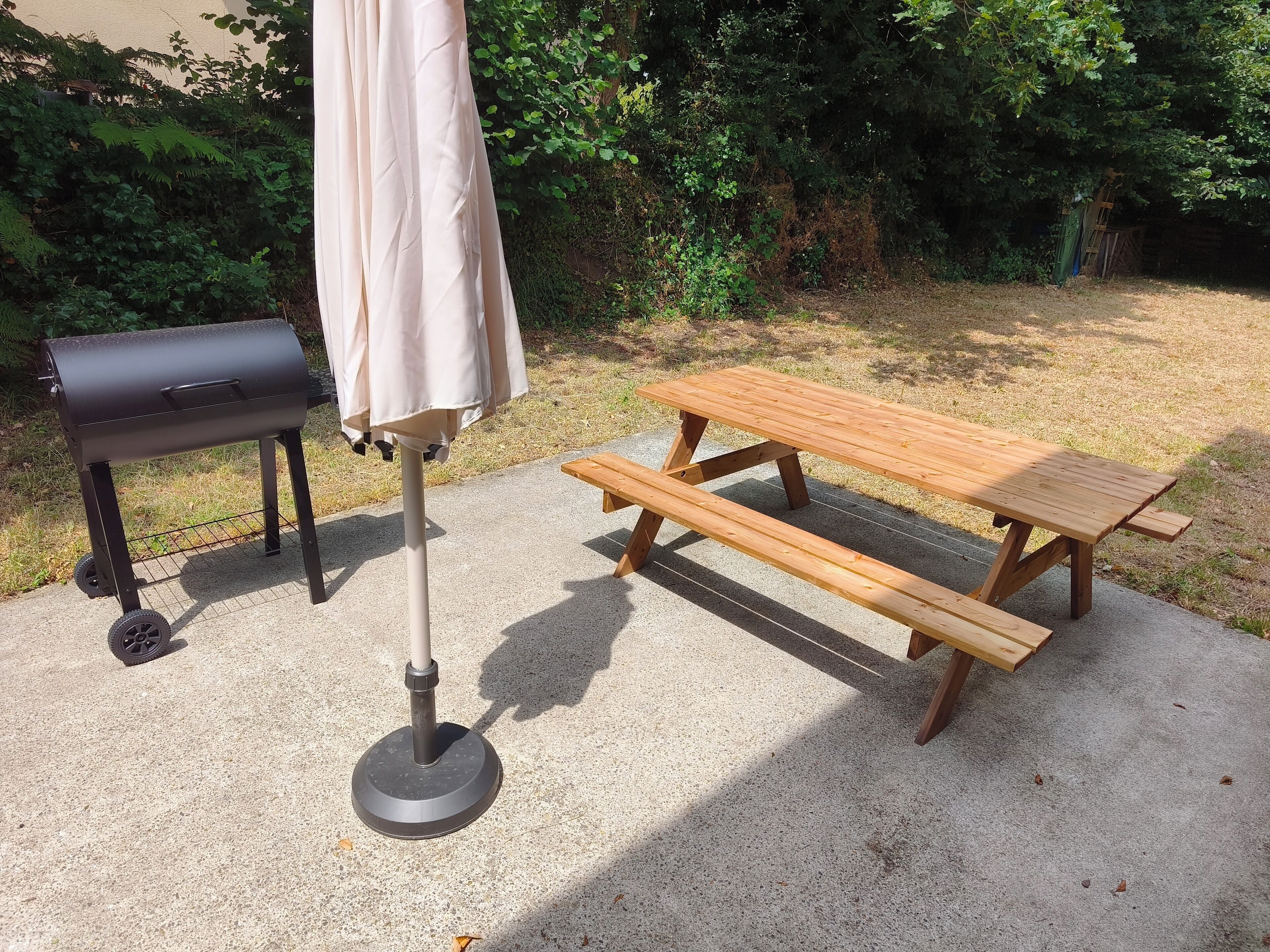 Un barbecue, une table de pique-nique et un parasol, le tout installé dans un jardin.