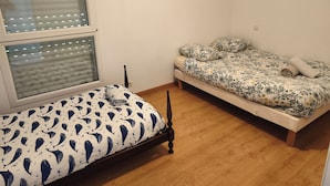 A bedroom with two beds, one with a patterned bedspread and the other with a solid color.