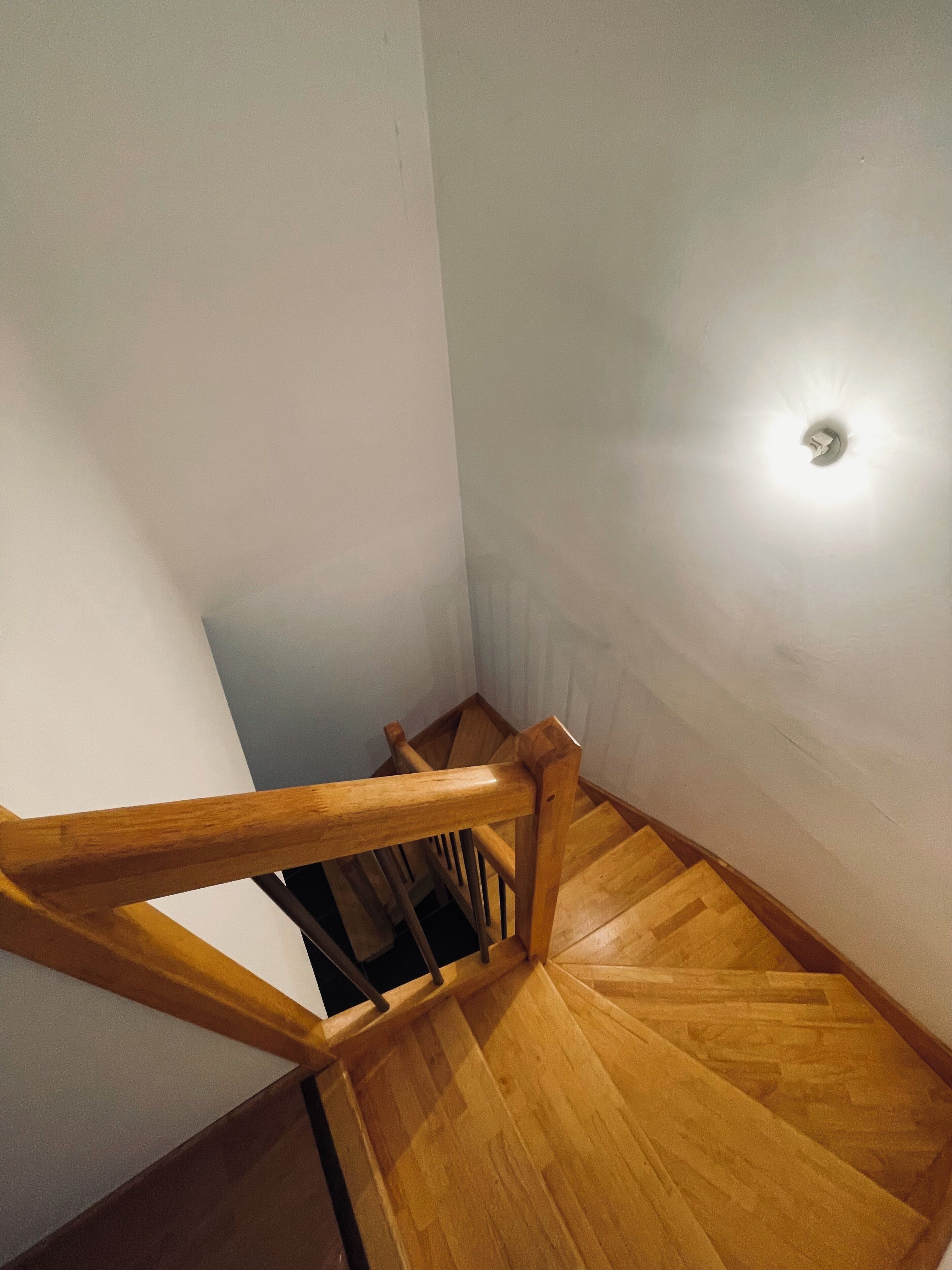A wooden staircase with a handrail and a light fixture on the wall.