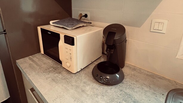 A kitchen with a microwave, coffee maker, and a small table with a towel.