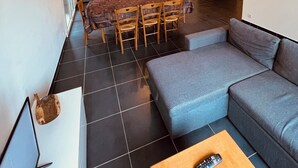 A modern living room with a grey sofa, a dining table with chairs, and a kitchen area in the background.
