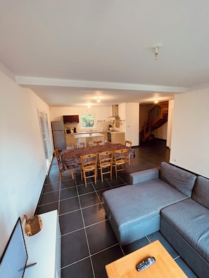 Una sala de estar moderna con un sofá gris, una mesa de comedor con sillas y una zona de cocina al fondo.