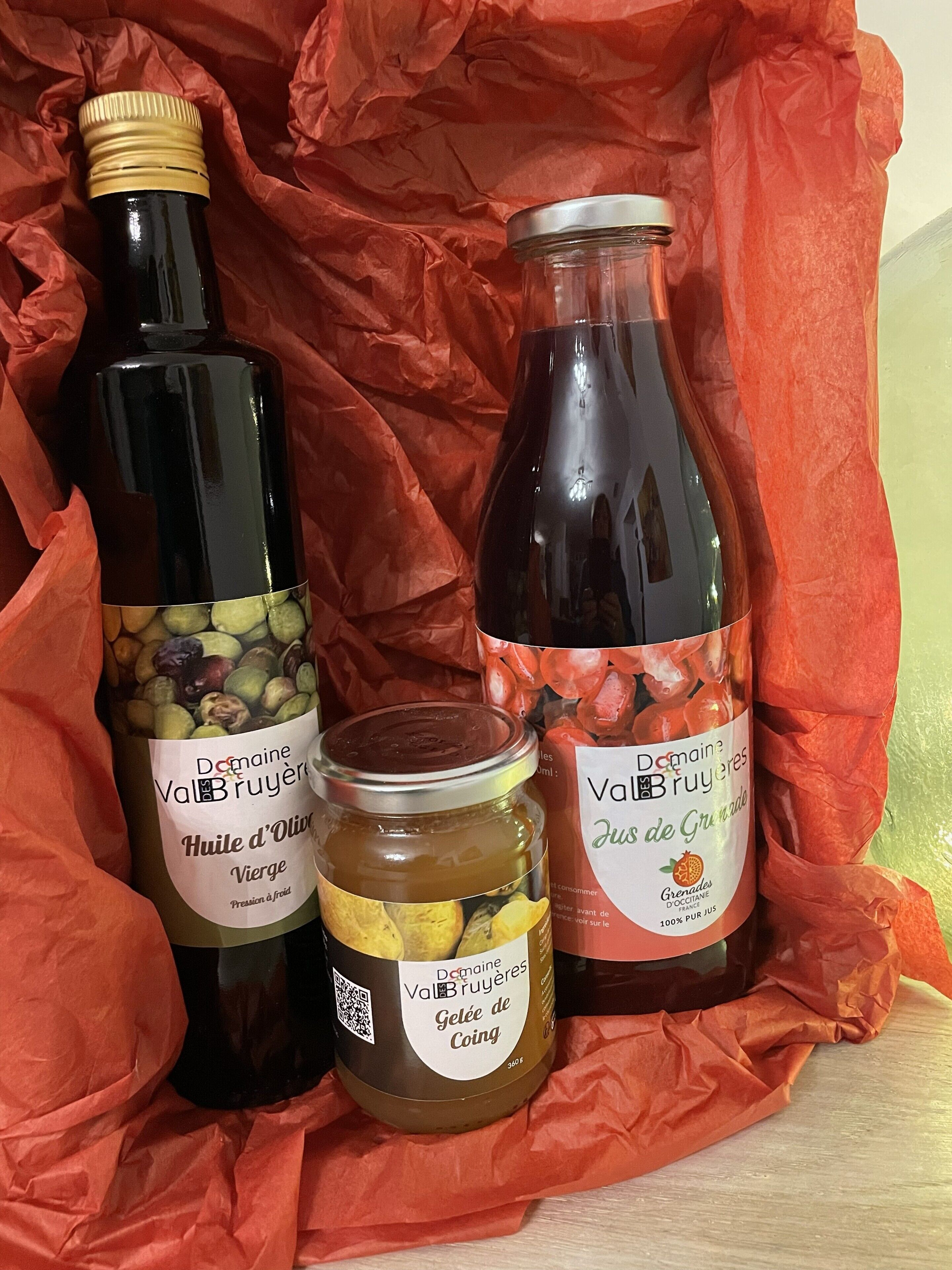 Three bottles of Val Bruyères wine, one with olives and one with grenades, on a red cloth.