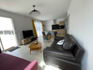 A modern living room with a leather sofa, a television, and a dining area with chairs and a table. - L'Olivier – A quiet, air-conditioned vacation rental in a traditional village near Pézenas (Neffiès)