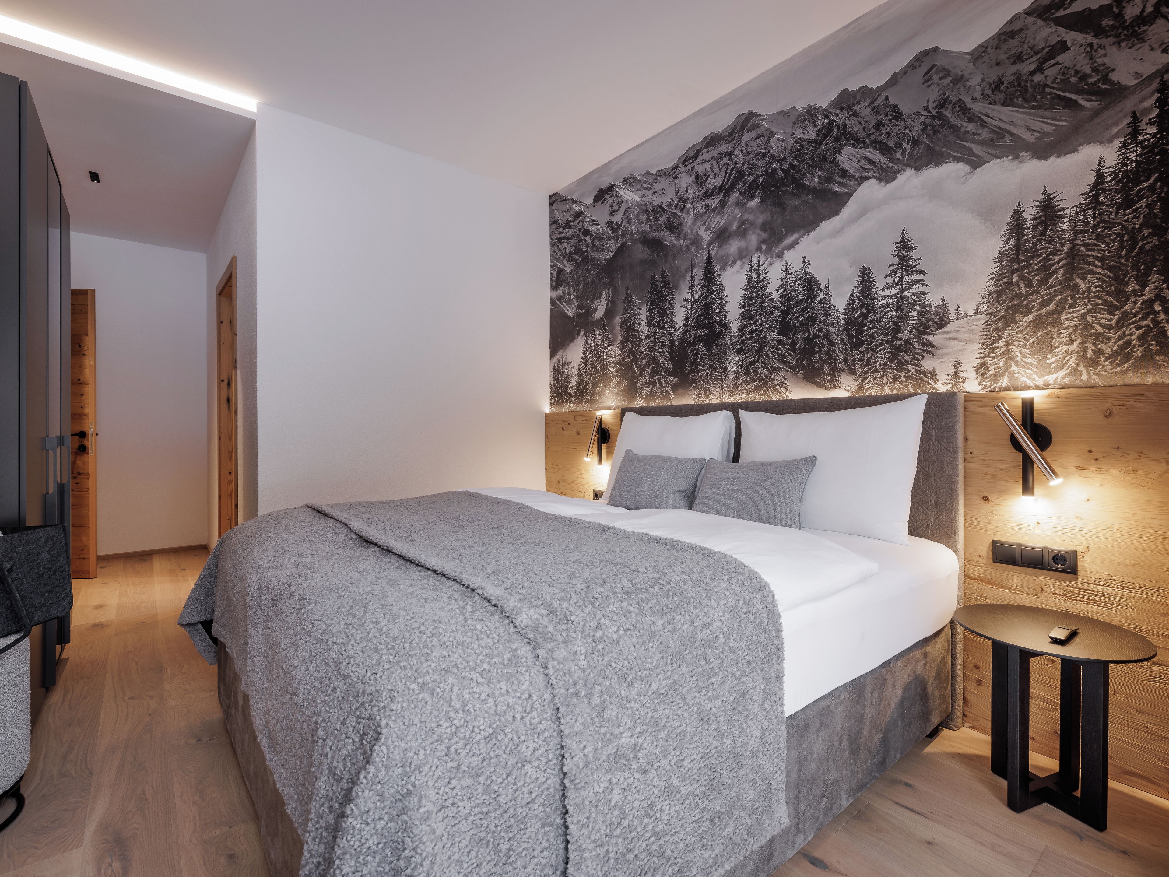 Une chambre dotée d’un grand lit, d’une tête de lit avec éclairage intégré, d’un téléviseur fixé au mur et d’une fresque représentant un paysage de montagne enneigé.