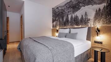Une chambre dotée d’un grand lit, d’une tête de lit avec éclairage intégré, d’un téléviseur fixé au mur et d’une fresque représentant un paysage de montagne enneigé.
